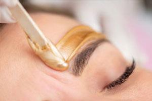 Eyebrow shape performed with hot wax. Beauty therapist applies hot wax to skin above eyebrow.